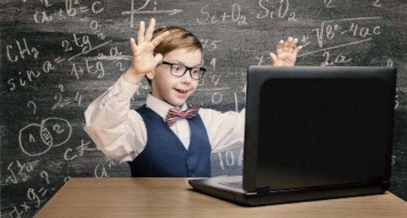 a happy boy in a classroom in front of a laptop, blackboard on the background with math problems