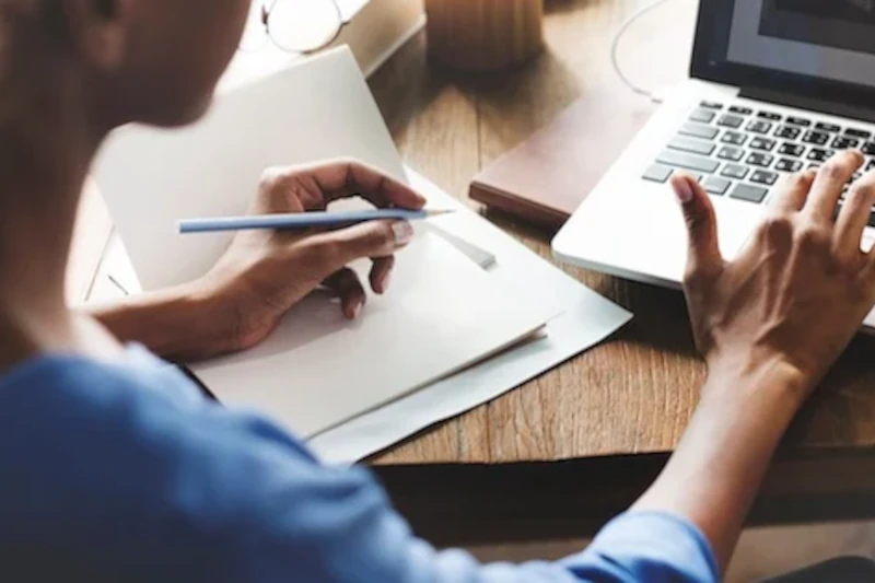 a person is working on a desk with laptop and a notebook