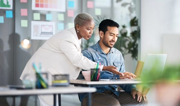colleagues conversing in the office at a desk with a laptop