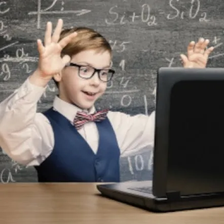 a happy boy in a classroom in front of a laptop, blackboard on the background with math problems