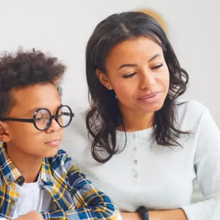 a mother helping her son studying, sitting on a desk with a laptop in front of them